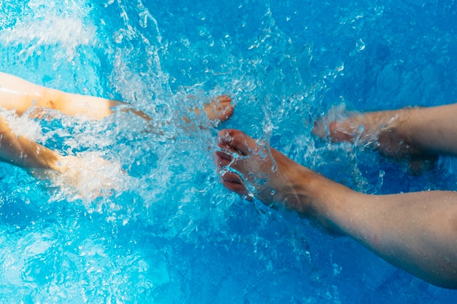 dva páry nohou šplouchající se v bazénu s průzračnou vodou